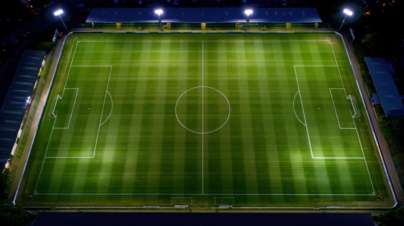 Aerial view of a soccer field at night illuminated by floodlights with striped grass and white markings