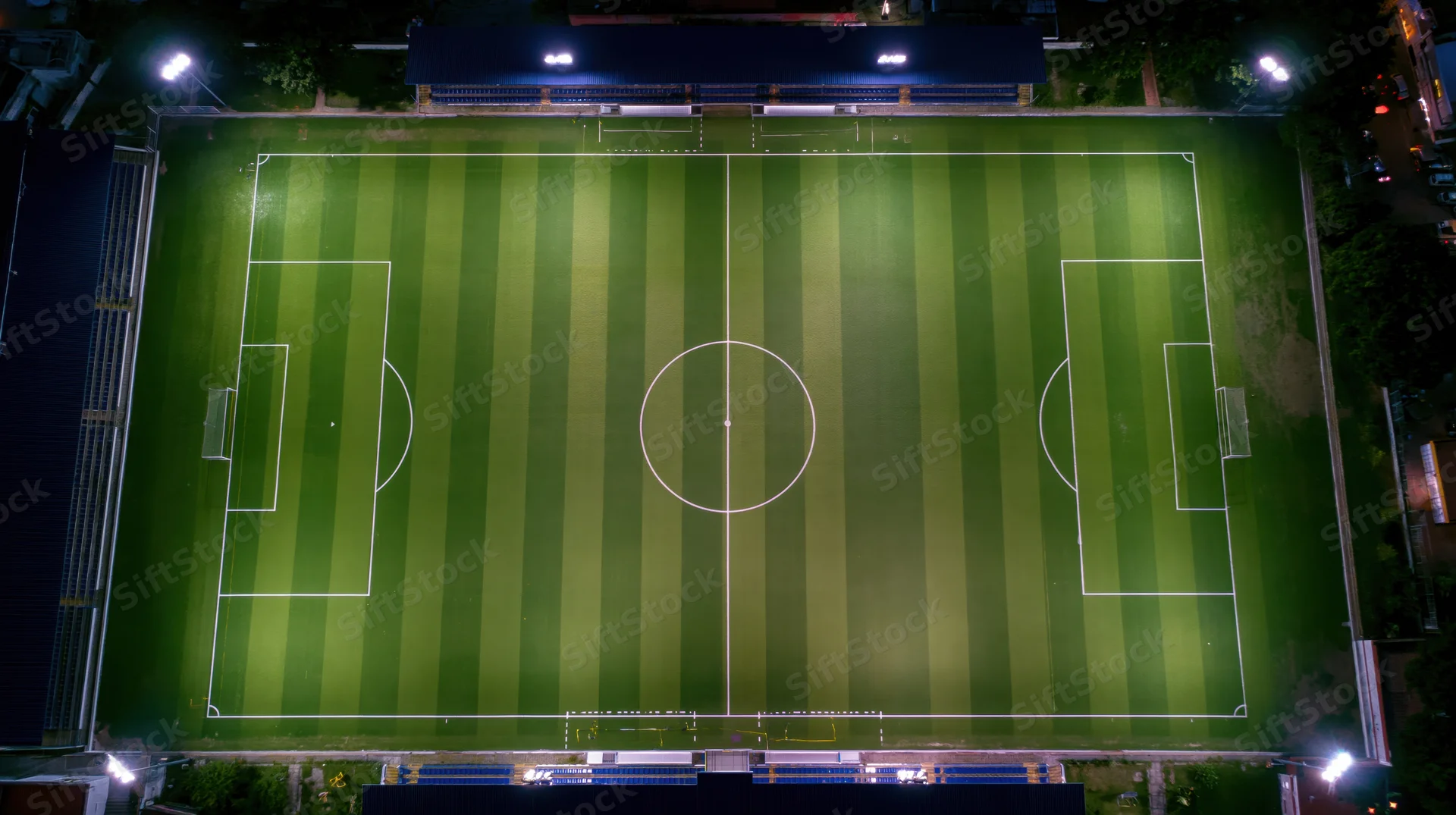 Aerial drone view of a striped soccer field at night illuminated by floodlights