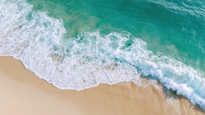 Aerial view of turquoise ocean waves breaking on sandy beach