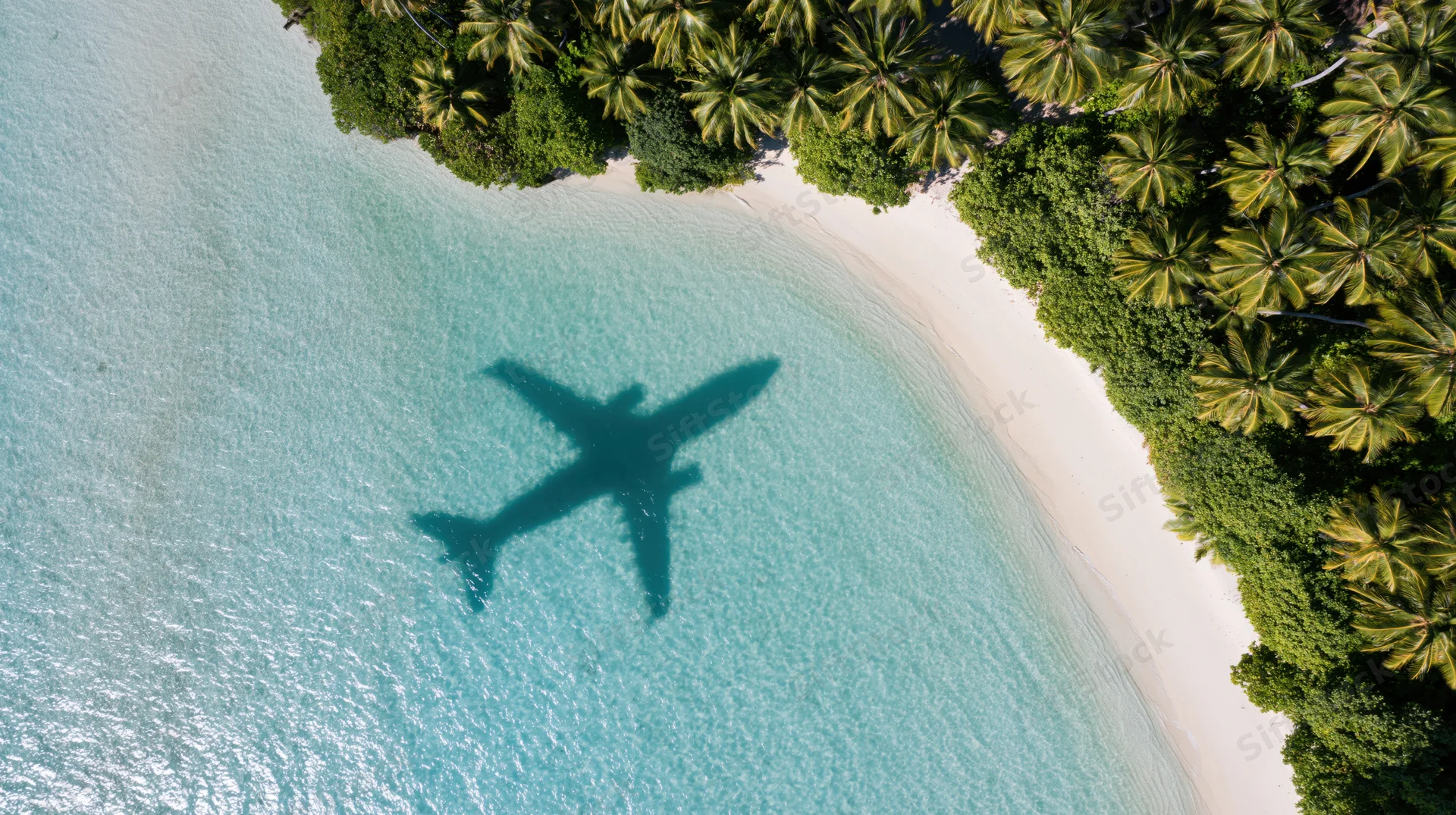 Aerial view of tropical island beach with airplane shadow on turquoise water