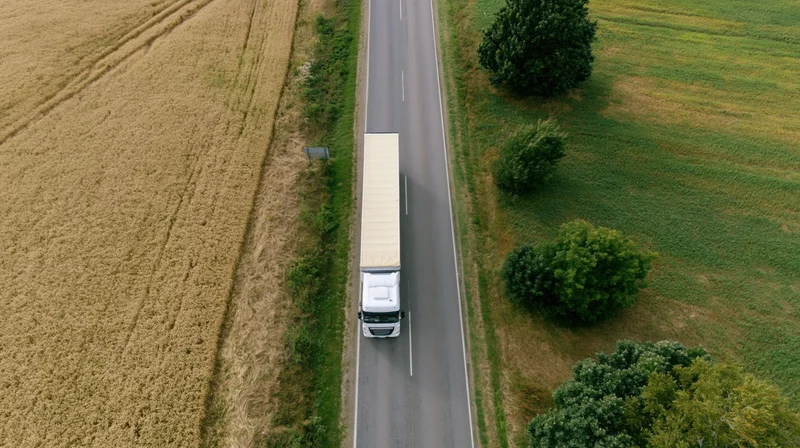 White semi-truck driving on a rural highway between golden wheat fields and green farmland