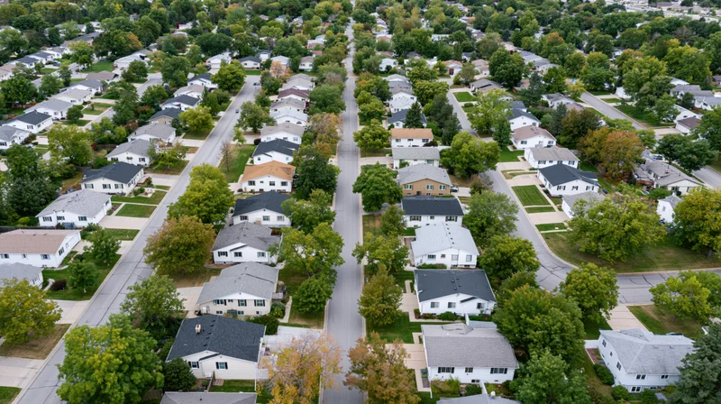 Aerial drone view of a suburban neighborhood with houses, trees, and streets arranged in a grid pattern