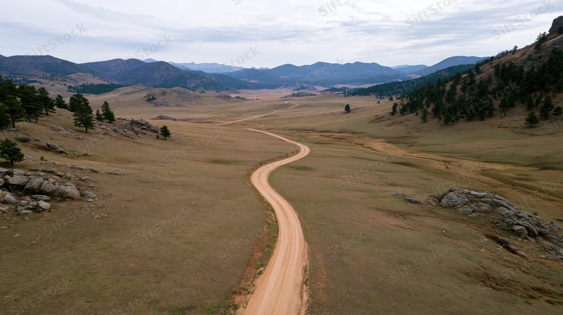Aerial view of a winding dirt road through a vast grassy valley surrounded by mountains