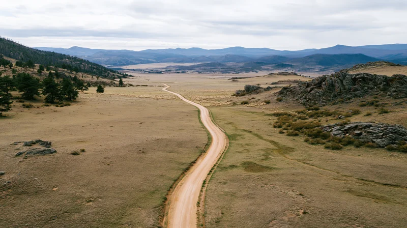 Winding dirt road through open grassland and rocky hills under overcast sky