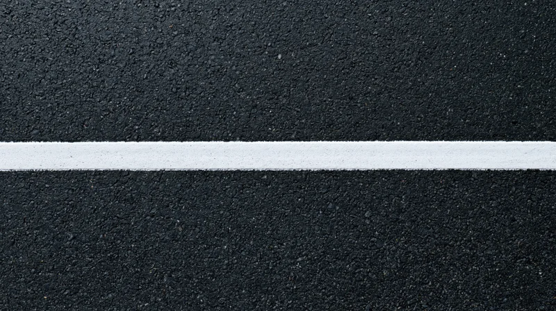 Aerial top-down close-up of dark asphalt road surface with a white painted line running horizontally across the frame