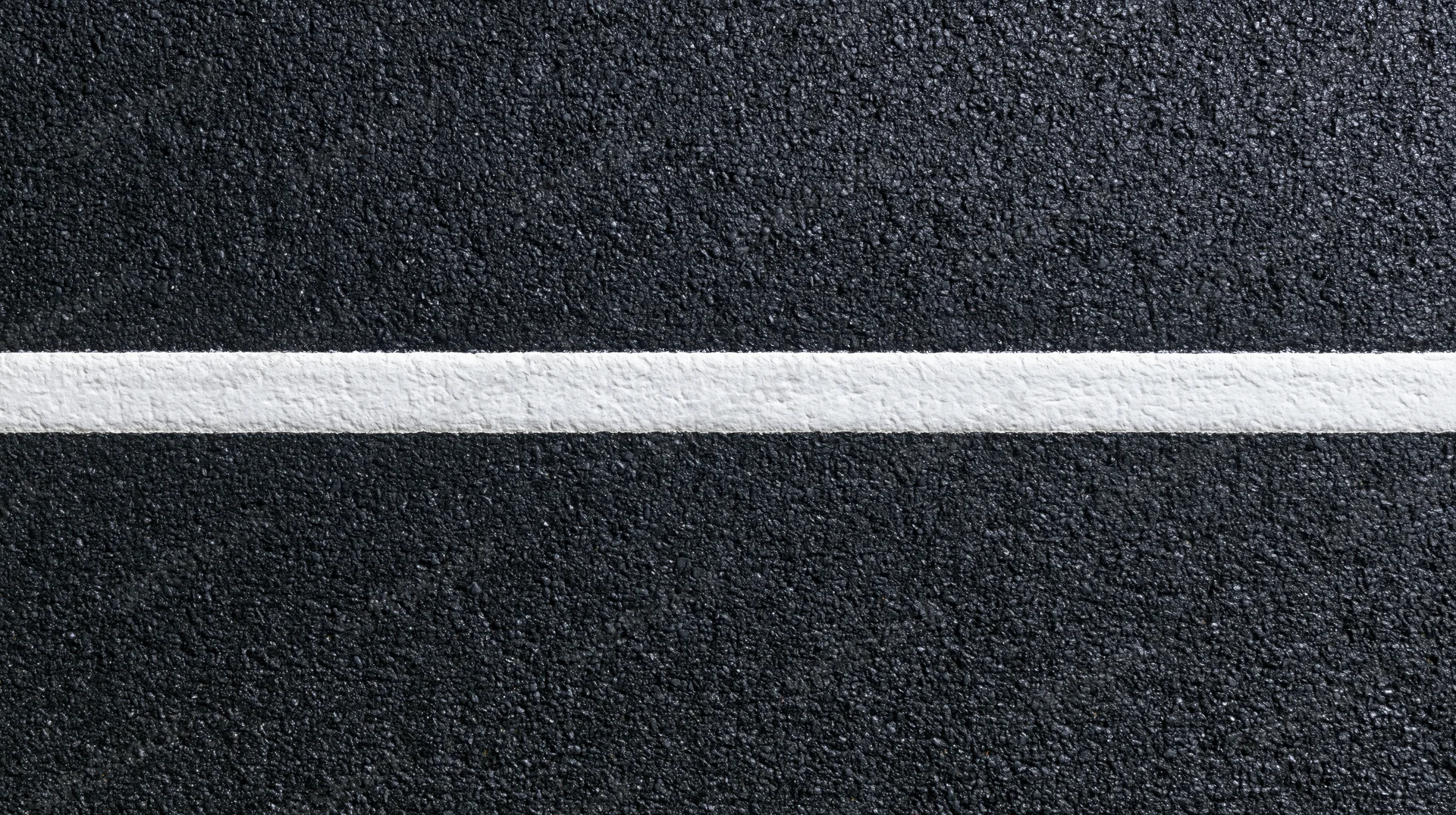 Aerial top-down close-up of dark asphalt road surface with a white painted line running horizontally across the frame