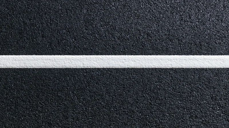 Aerial top-down close-up of dark asphalt road surface with a white painted line running horizontally across the frame