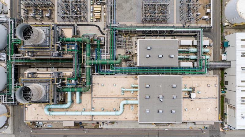 Aerial top-down view of industrial power plant with cooling towers and green pipelines