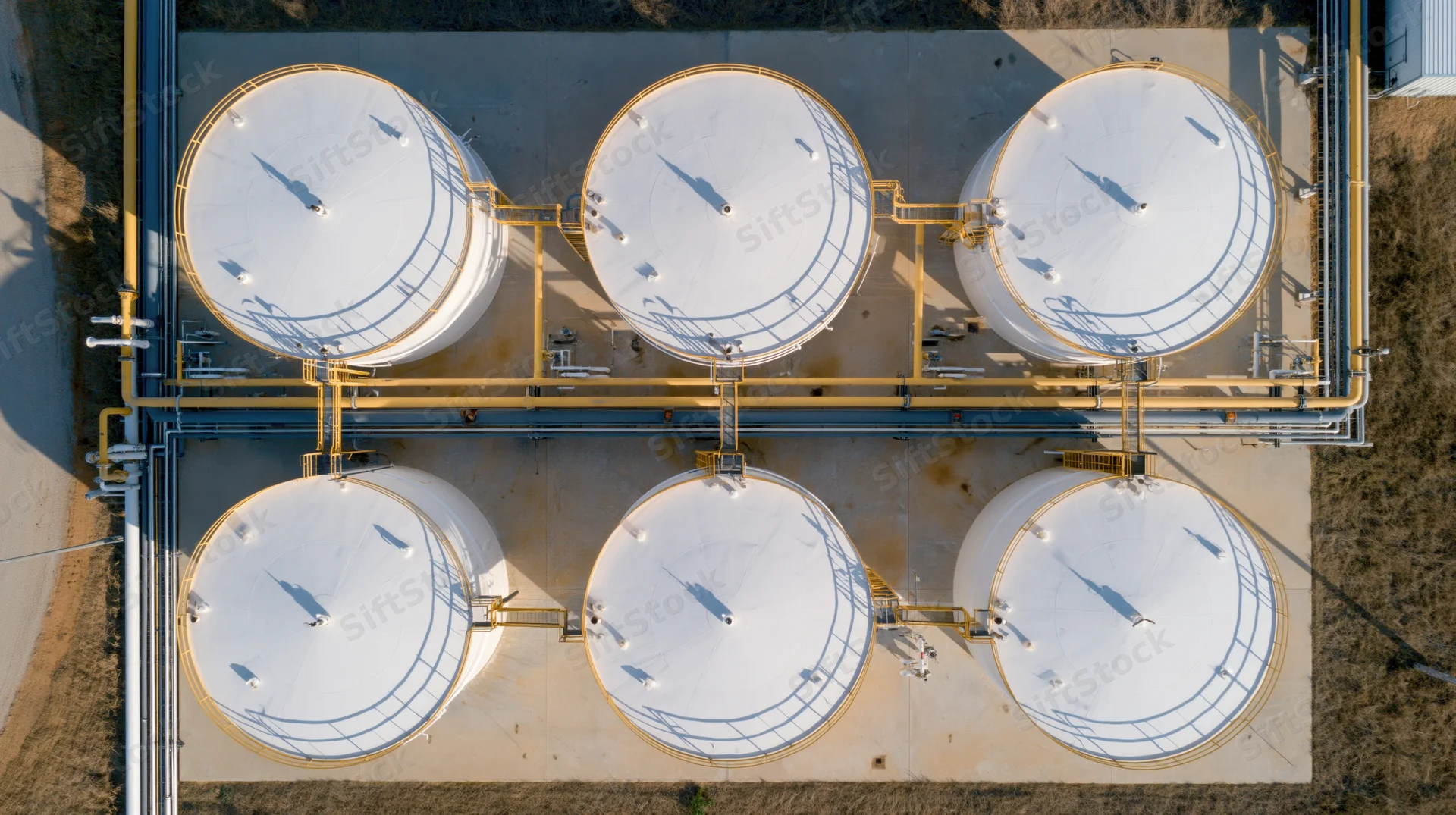 Aerial top-down view of six large white storage tanks arranged in two rows at an industrial facility with connecting pipes and valves