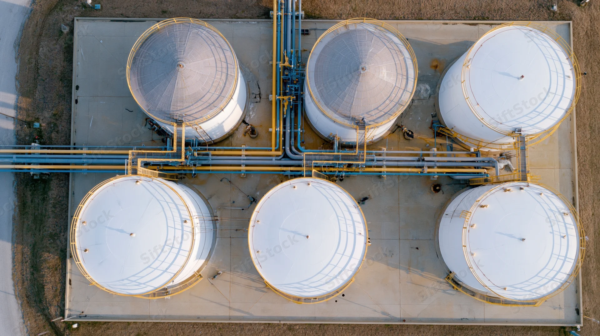 Aerial top-down view of six large white storage tanks arranged in two rows connected by pipelines at an industrial facility
