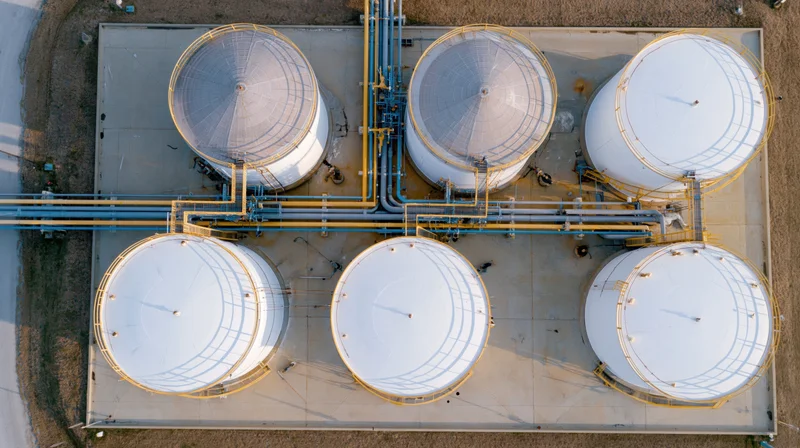 Aerial top-down view of six large white storage tanks arranged in two rows connected by pipelines at an industrial facility