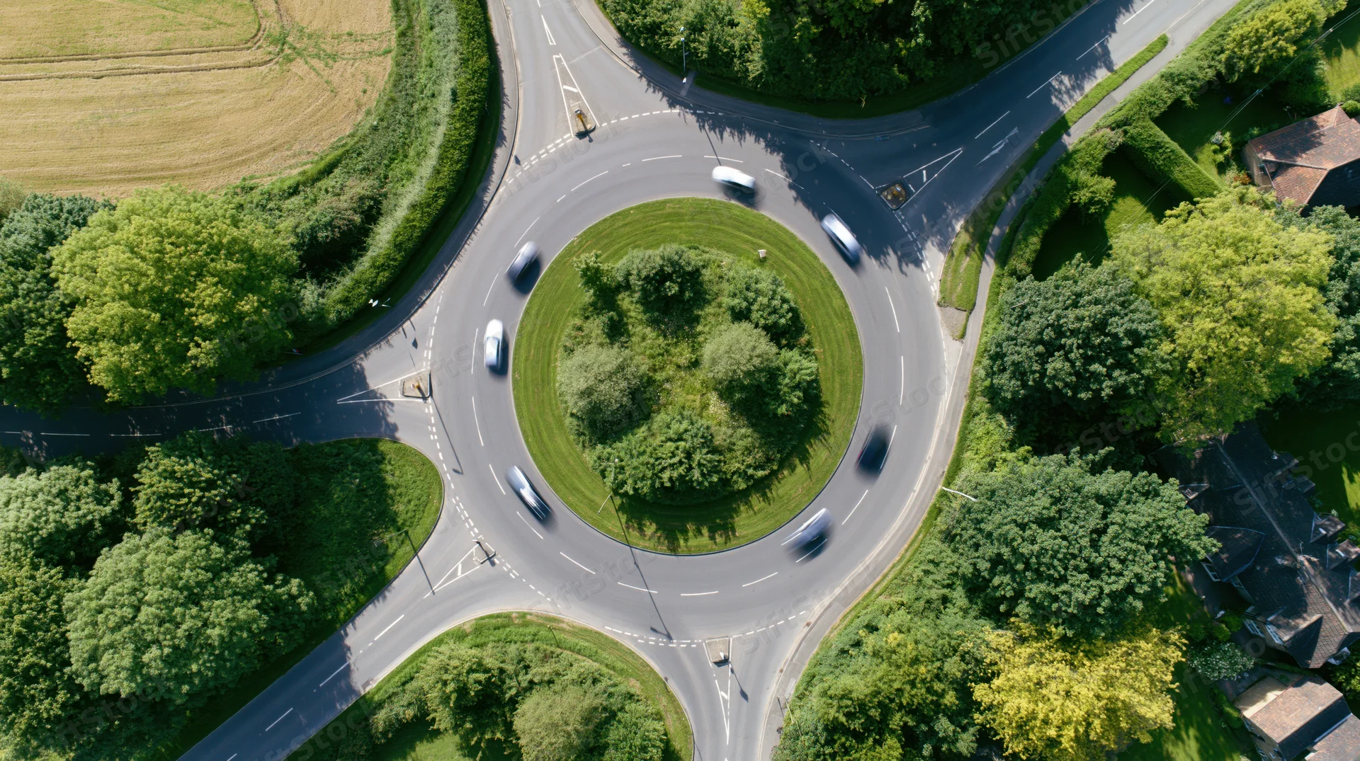 Aerial top-down view of a british roundabout with cars in motion surrounded by greenery and rural landscape
