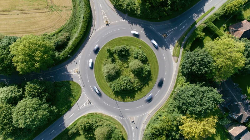 Aerial top-down view of a british roundabout with cars in motion surrounded by greenery and rural landscape