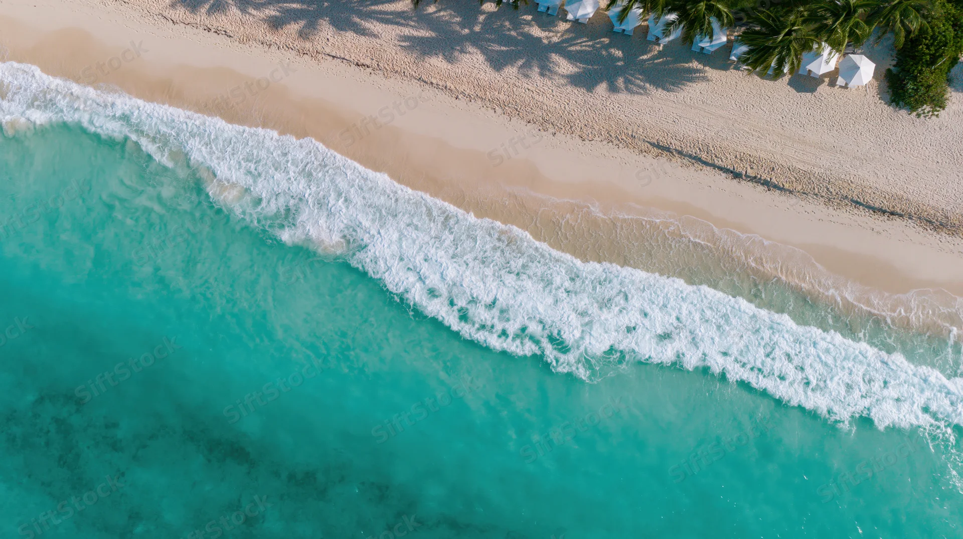 Aerial top-down view of turquoise ocean waves meeting sandy beach lined with palm trees and white umbrellas