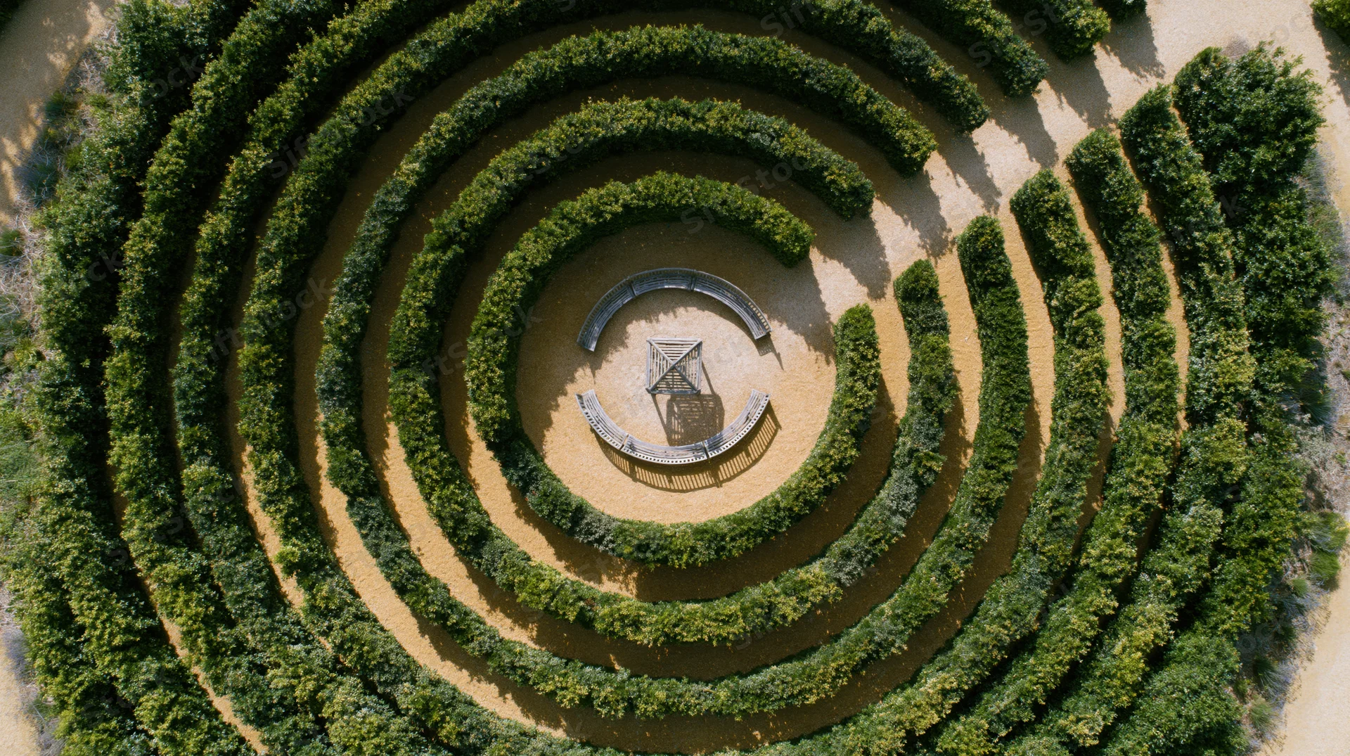 Aerial top-down view of a circular hedge labyrinth garden with a central amphitheater structure