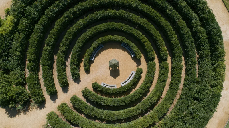 Aerial top-down view of a circular formal garden labyrinth with hedges, benches, and a central gazebo