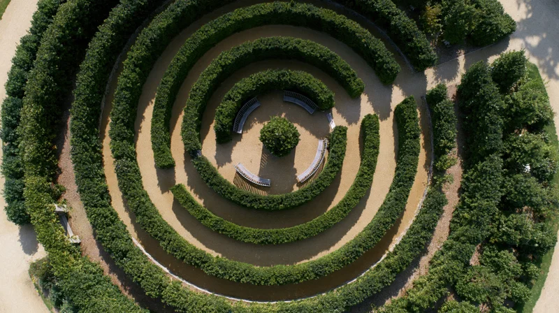 Aerial top-down view of a circular formal garden labyrinth with spiral hedge paths and central tree