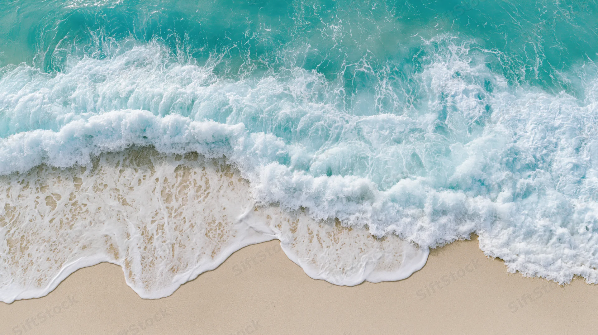 Aerial top-down view of a gentle ocean wave breaking on a sandy beach