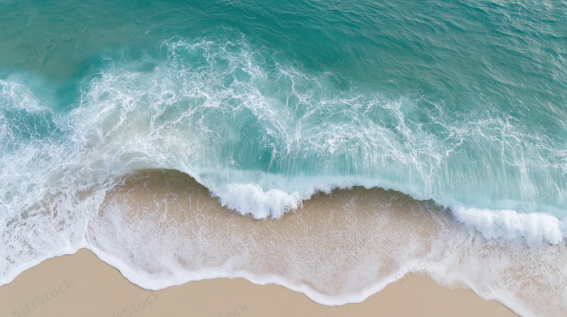 Aerial top-down view of a gentle ocean wave breaking on sandy beach
