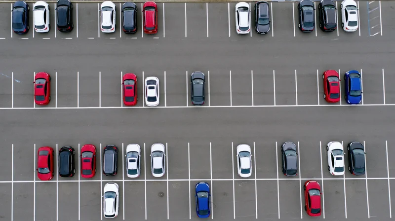 Aerial top-down view of a large asphalt parking lot filled with parked cars arranged in rows