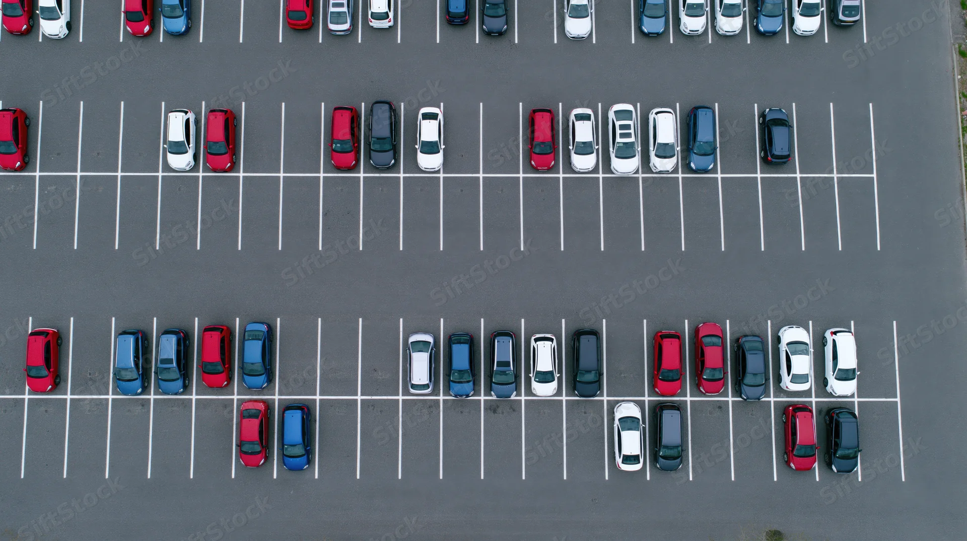 Aerial top-down view of a large asphalt parking lot filled with parked cars arranged in rows