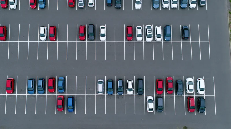 Aerial top-down view of a large asphalt parking lot filled with parked cars arranged in rows