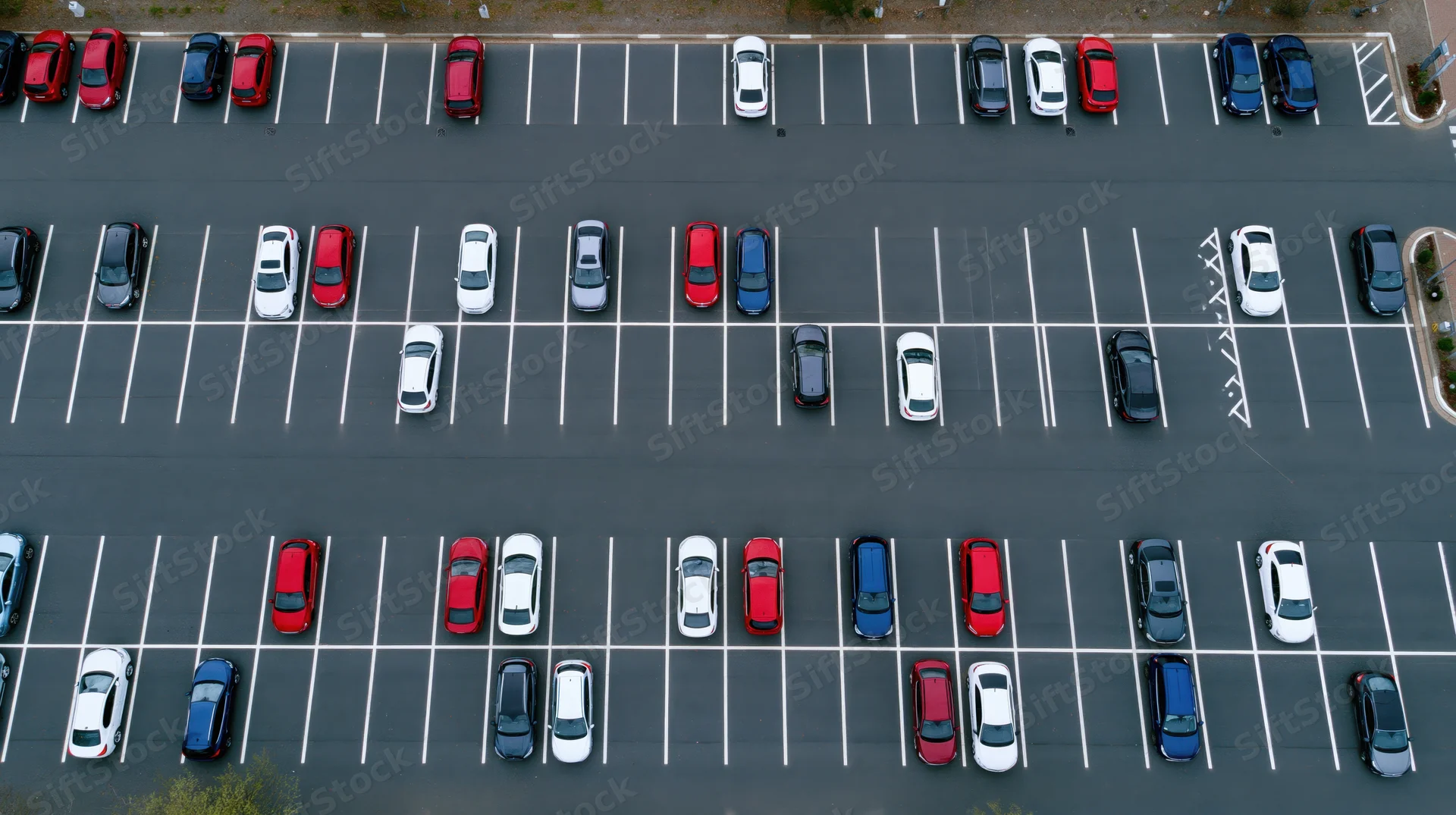 Aerial top-down view of a large asphalt parking lot filled with parked cars arranged in rows