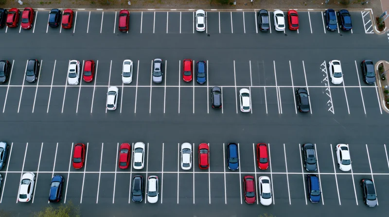 Aerial top-down view of a large asphalt parking lot filled with parked cars arranged in rows