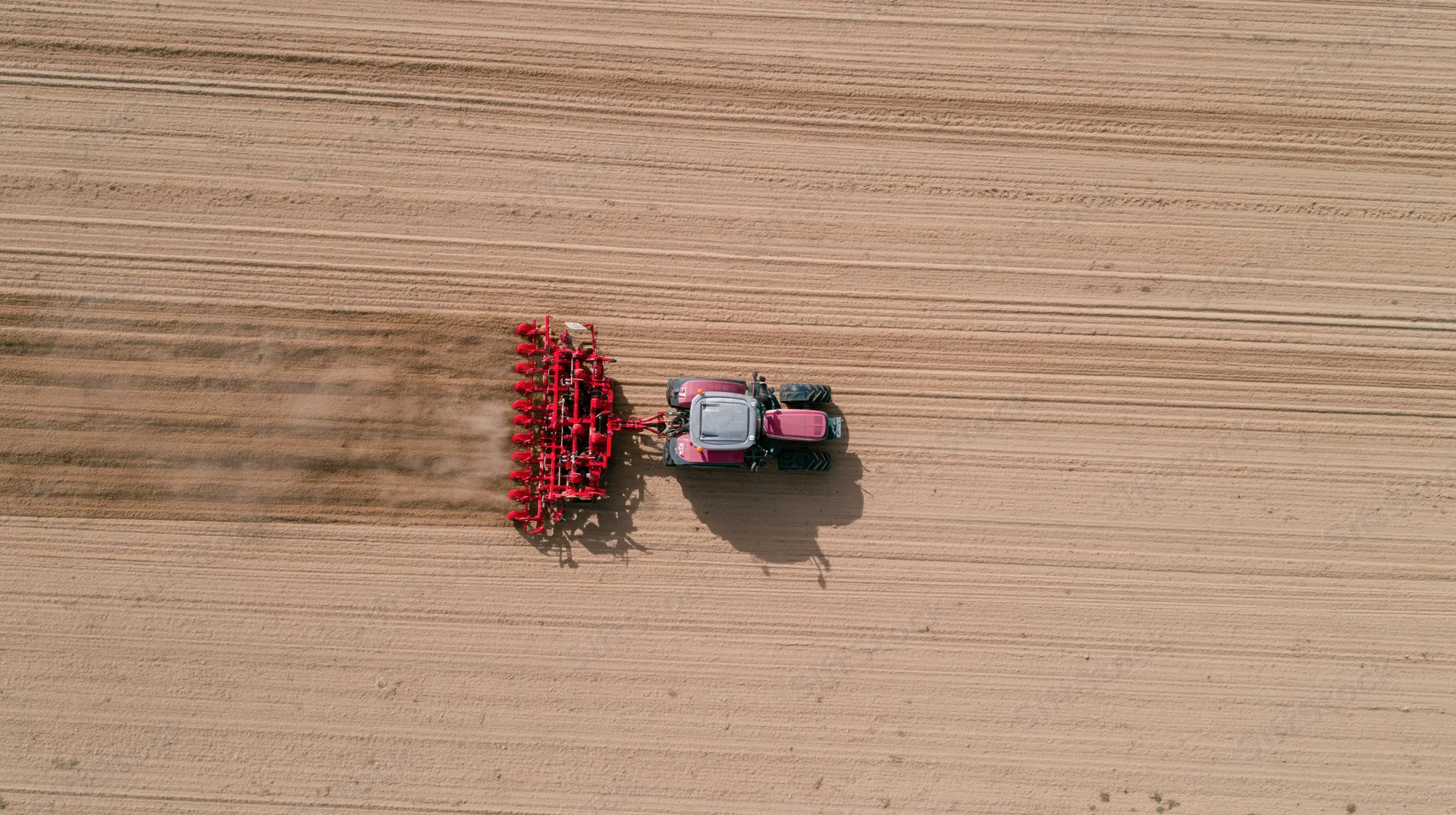 Aerial top-down of pink and grey tractor pulling red implement