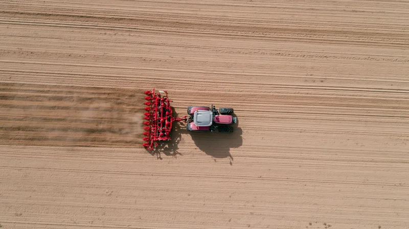 Aerial top-down of pink and grey tractor pulling red implement