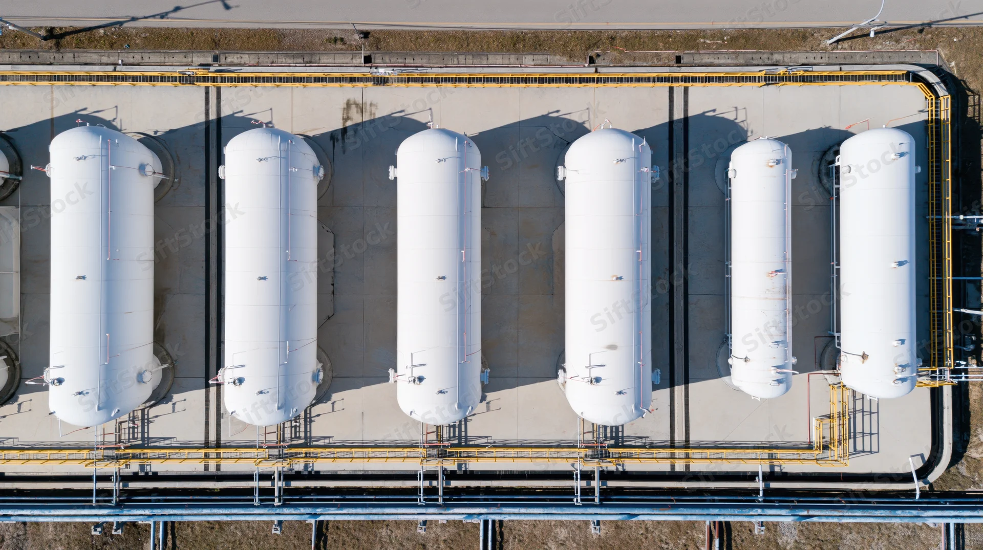 Aerial top-down view of six white cylindrical storage tanks in a row at an industrial facility