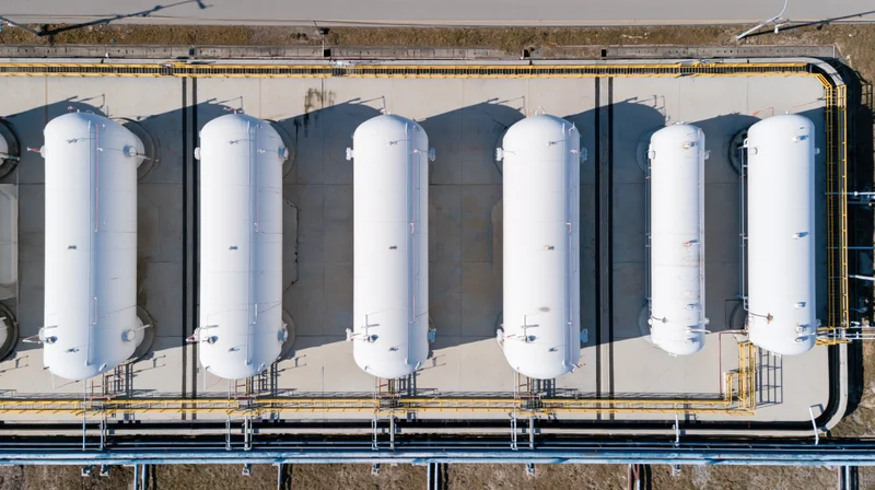 Aerial top-down view of six white cylindrical storage tanks in a row at an industrial facility