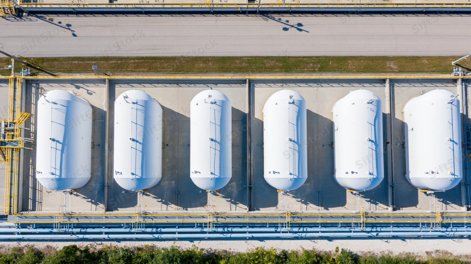 Aerial top-down view of six white cylindrical storage tanks in a row at an industrial facility