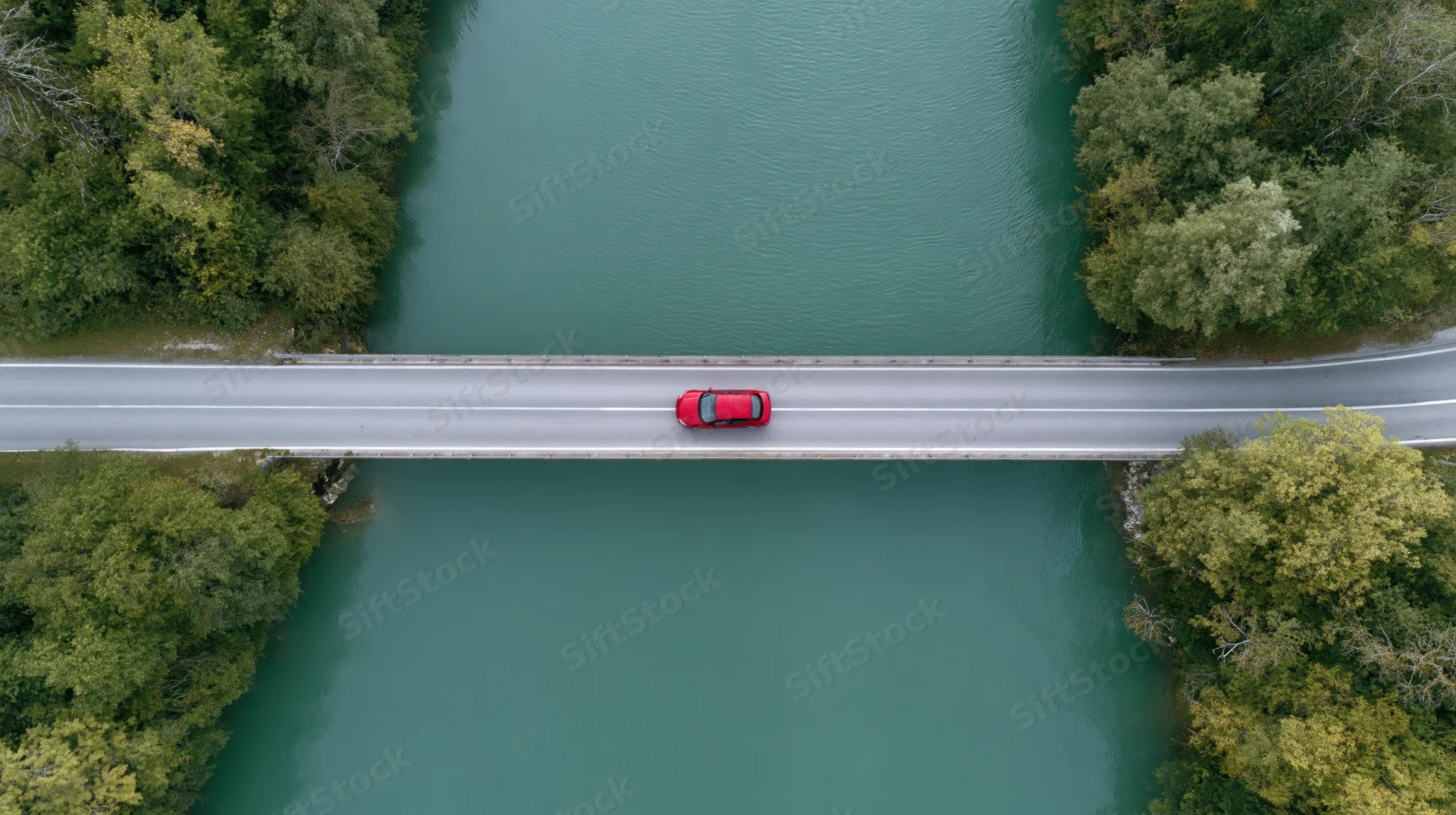 Red car driving across bridge over river from aerial top-down view