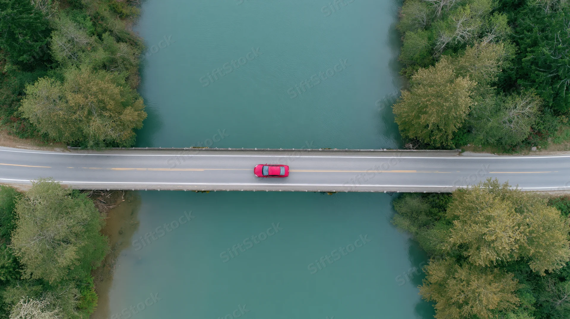 Red car driving across a bridge over a river from an aerial top-down view