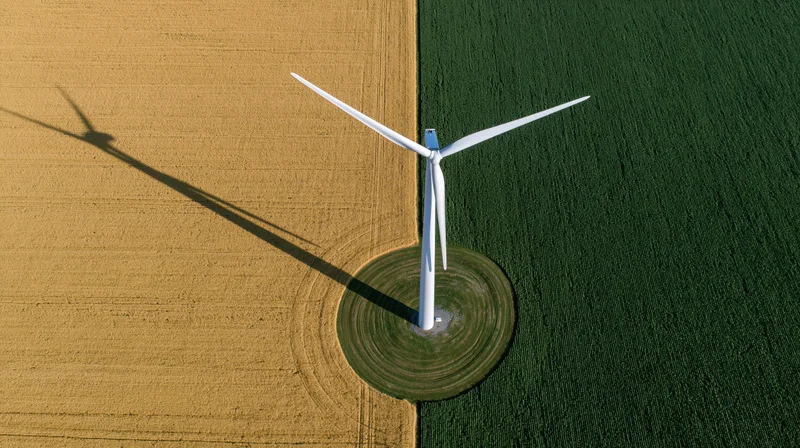 Aerial top-down view of a single white wind turbine standing between golden and green agricultural fields