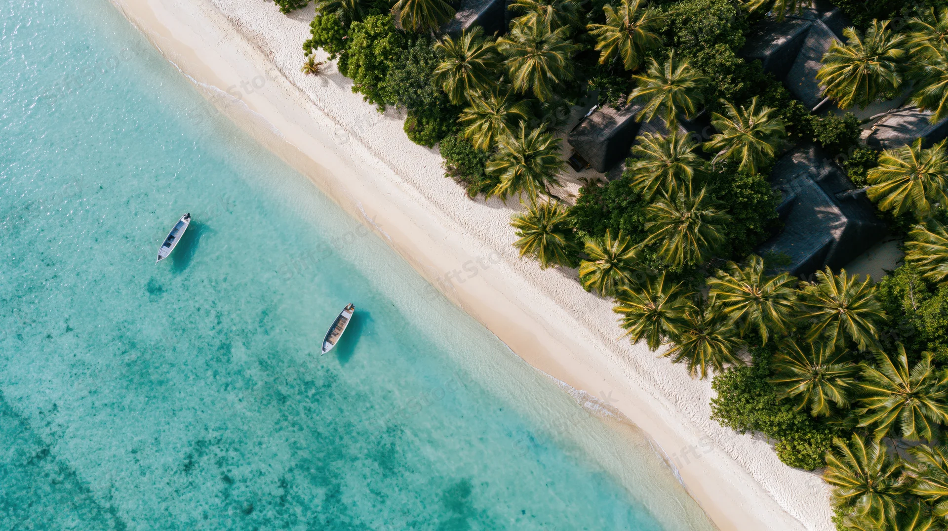 Aerial top-down view of a tropical beach resort with white sand, turquoise water, palm trees, and boats near the shoreline