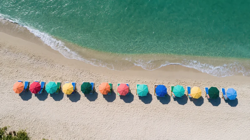 Colorful umbrellas and deckchairs lined along a tropical beach shoreline with turquoise ocean waves