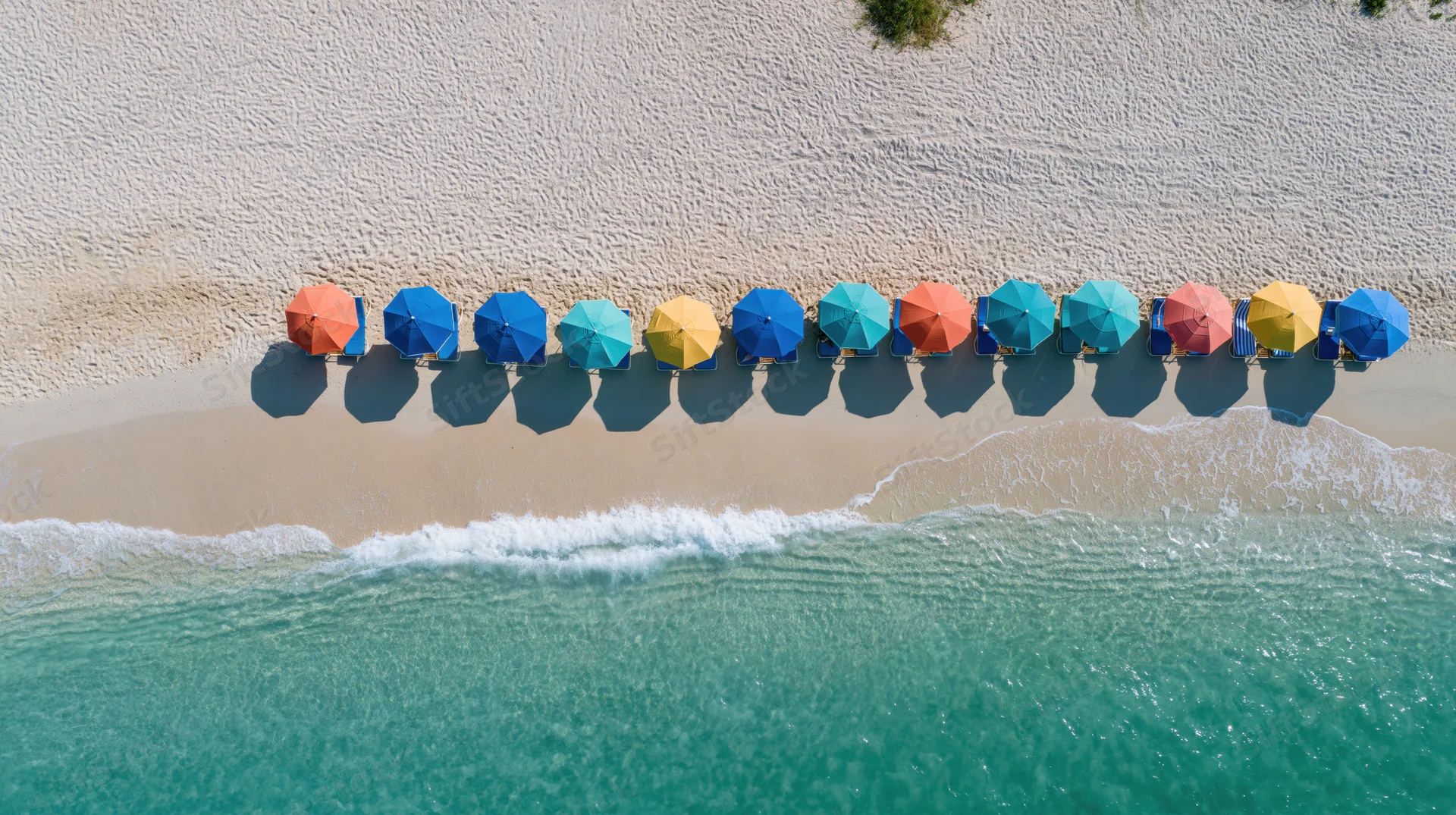 Row of colorful umbrellas along tropical beach shoreline from aerial view