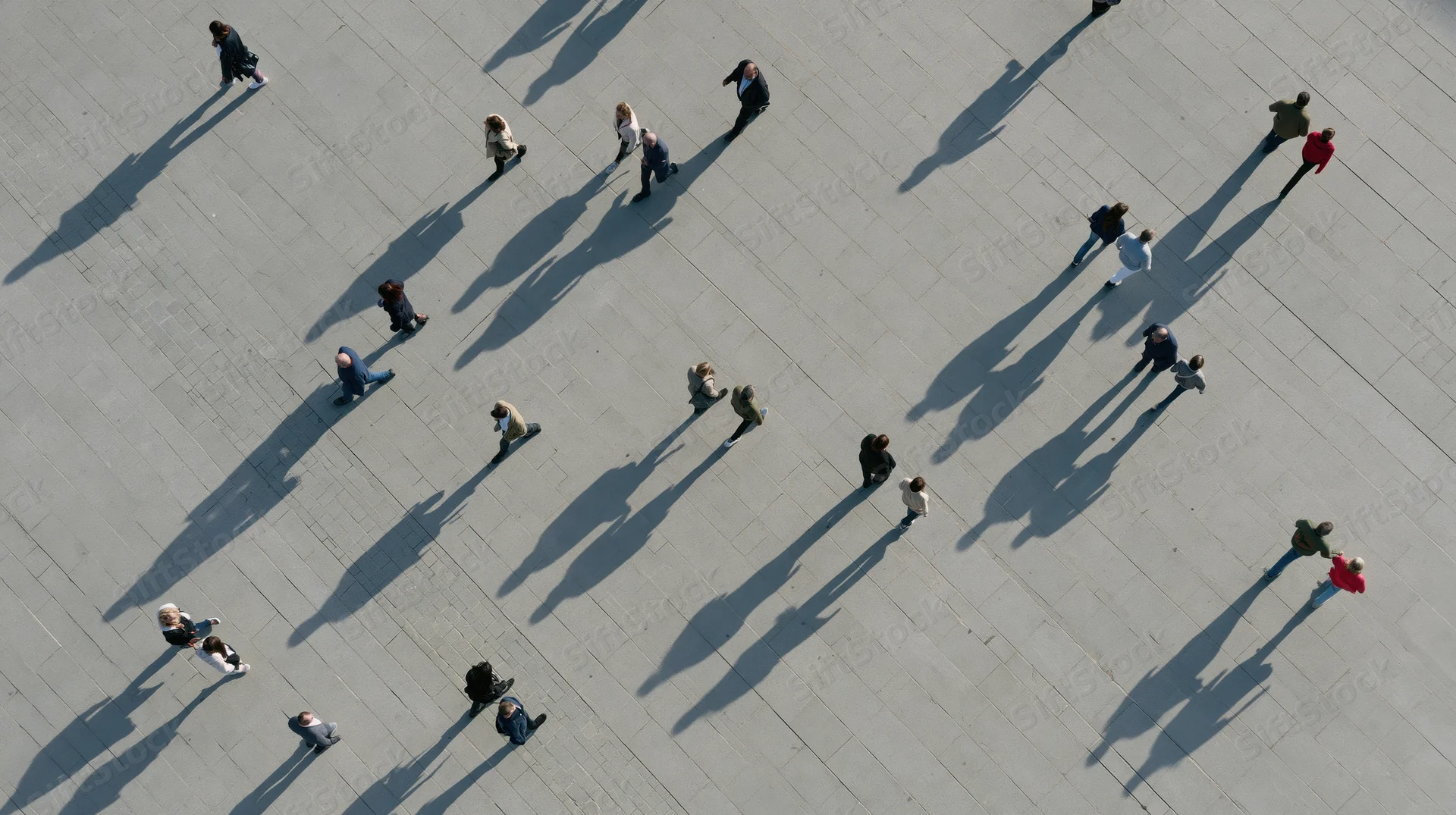 Aerial top-down view of pedestrians walking across a paved urban plaza