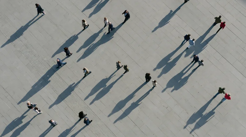 Aerial top-down view of pedestrians walking across a paved urban plaza