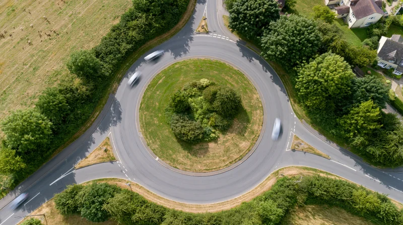 Aerial top-down view of a roundabout with moving vehicles surrounded by greenery and suburban homes