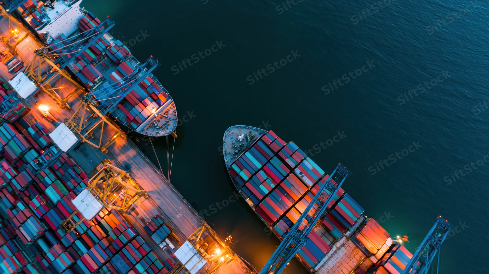 Aerial top-down view of container ships docked at a busy commercial port at night with cranes loading cargo