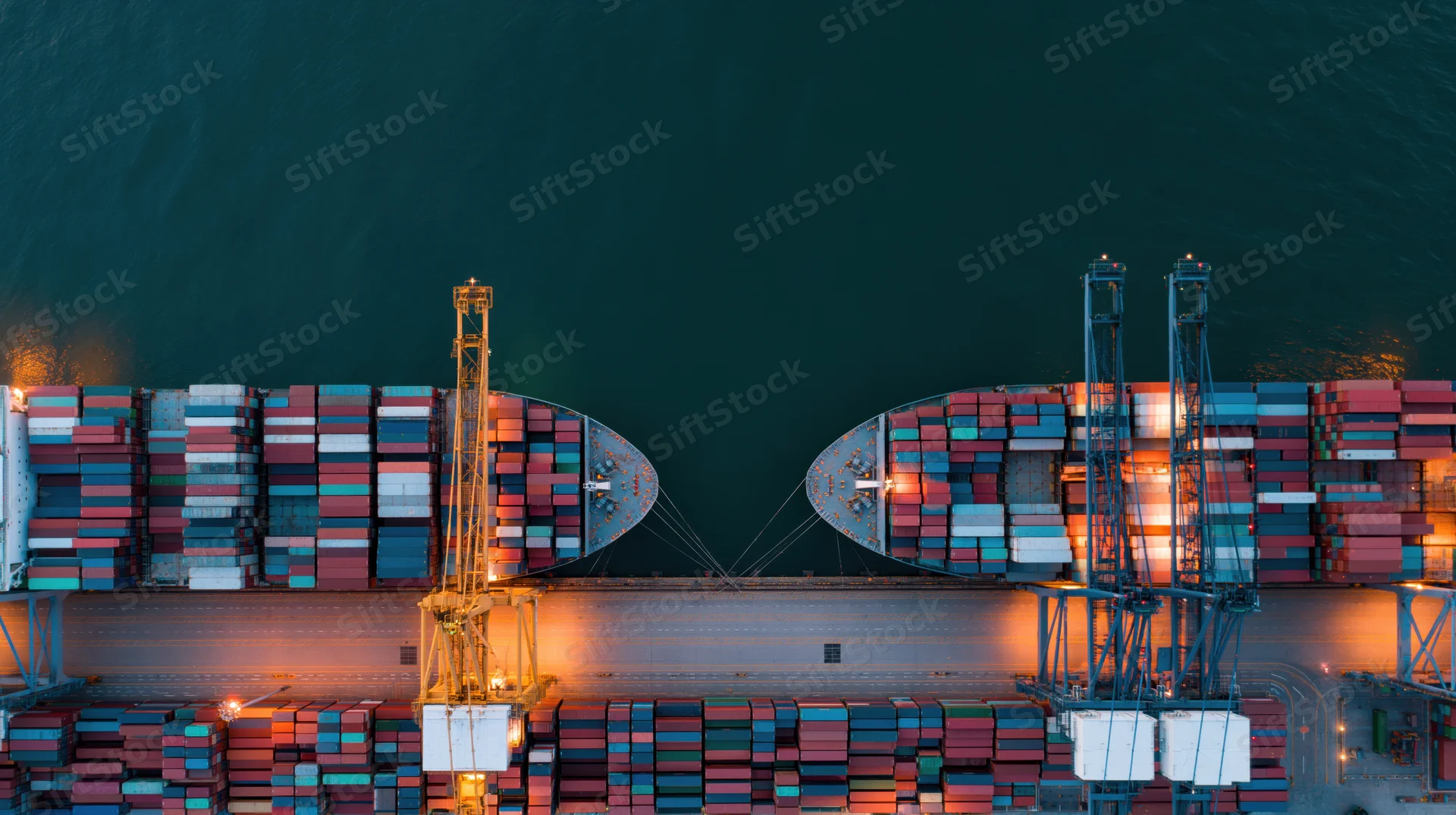 Aerial top-down view of two container ships docked at a commercial port with cranes loading cargo at night