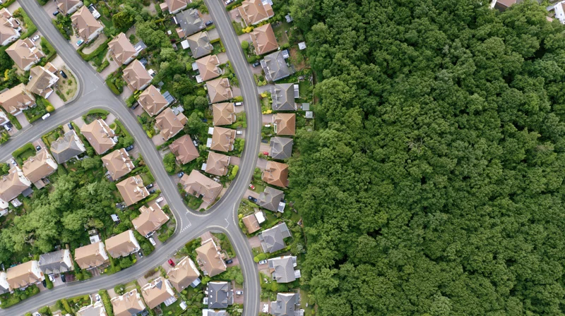 Aerial top-down view of a dense british residential suburb with winding streets and green forest border