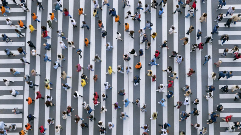 Aerial top-down view of dense crowd of pedestrians crossing city street crosswalk