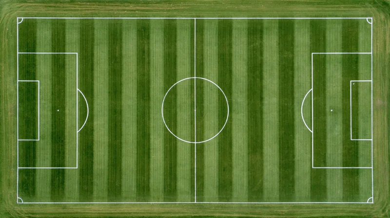 Aerial top-down view of a full soccer field with white painted lines on striped green grass