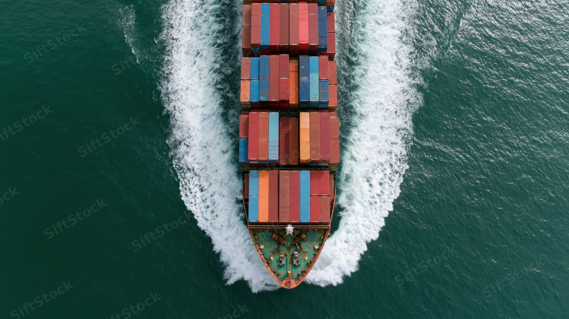 Aerial top-down view of a large cargo container ship moving through the ocean leaving a white wake
