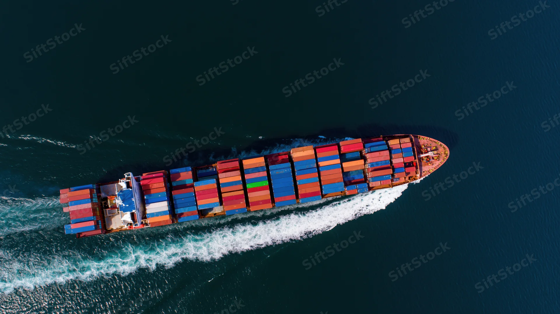 Large cargo container ship moving across ocean from aerial top-down view