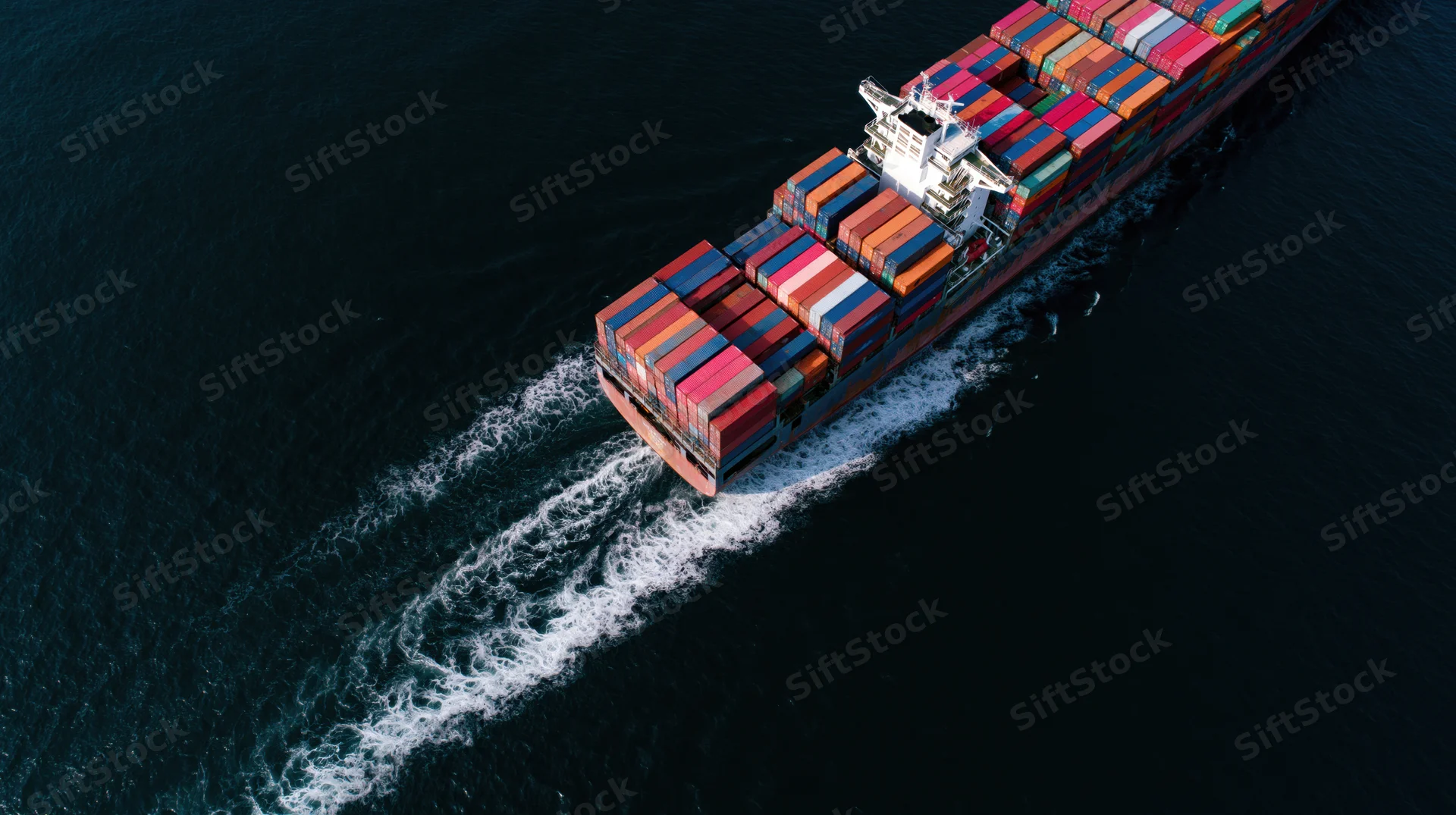 Large cargo container ship moving across dark ocean leaving white wake